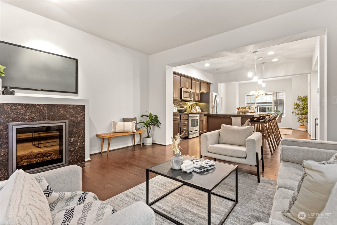 Modern living room with fireplace, sofa, coffee table, and kitchen in the background.