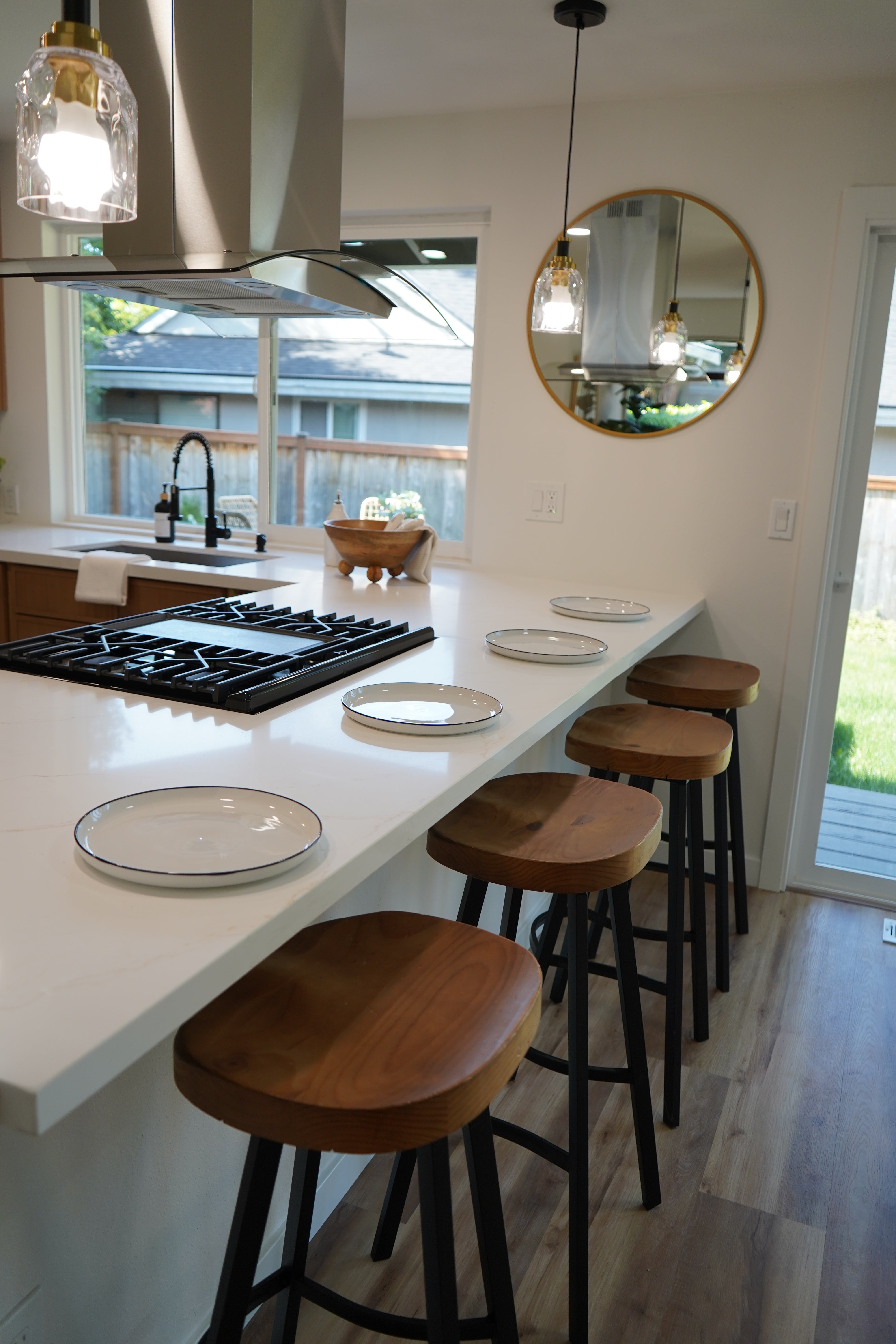 Modern kitchen with white island, wooden stools, and a round mirror.