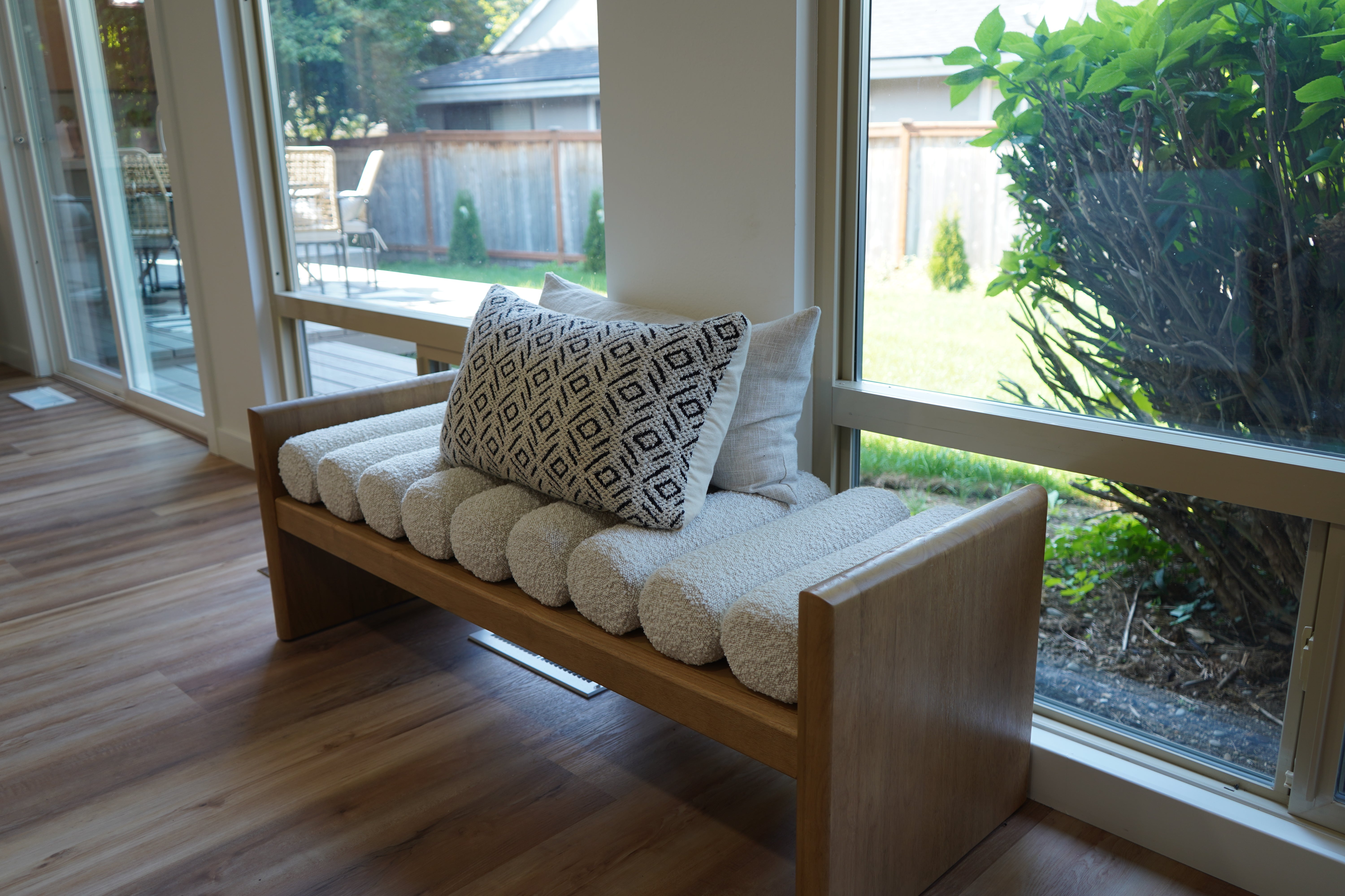 Wooden bench with cushions and pillows in a room with large windows.