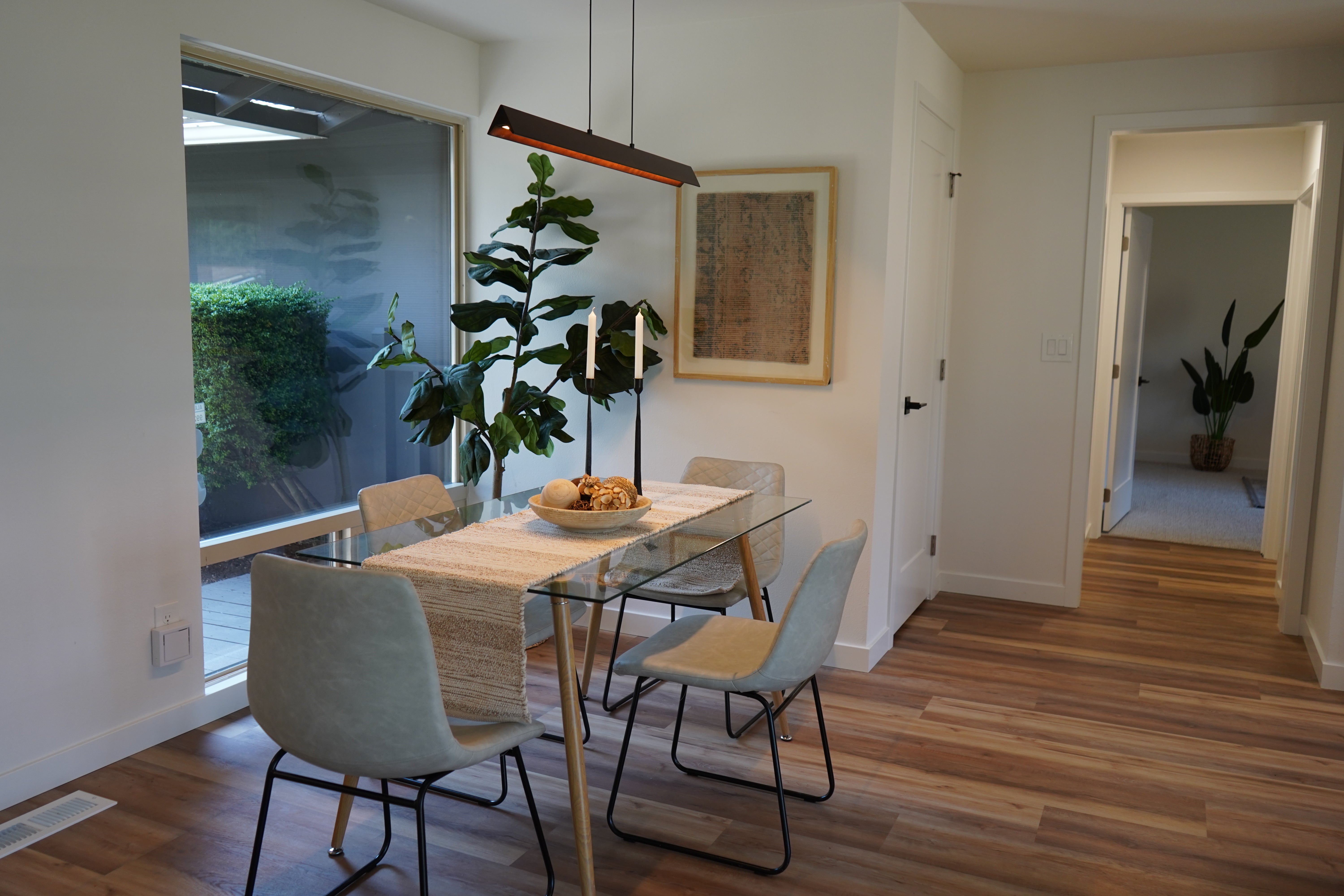 Modern dining room with a wooden table and chairs, large window, and plants.