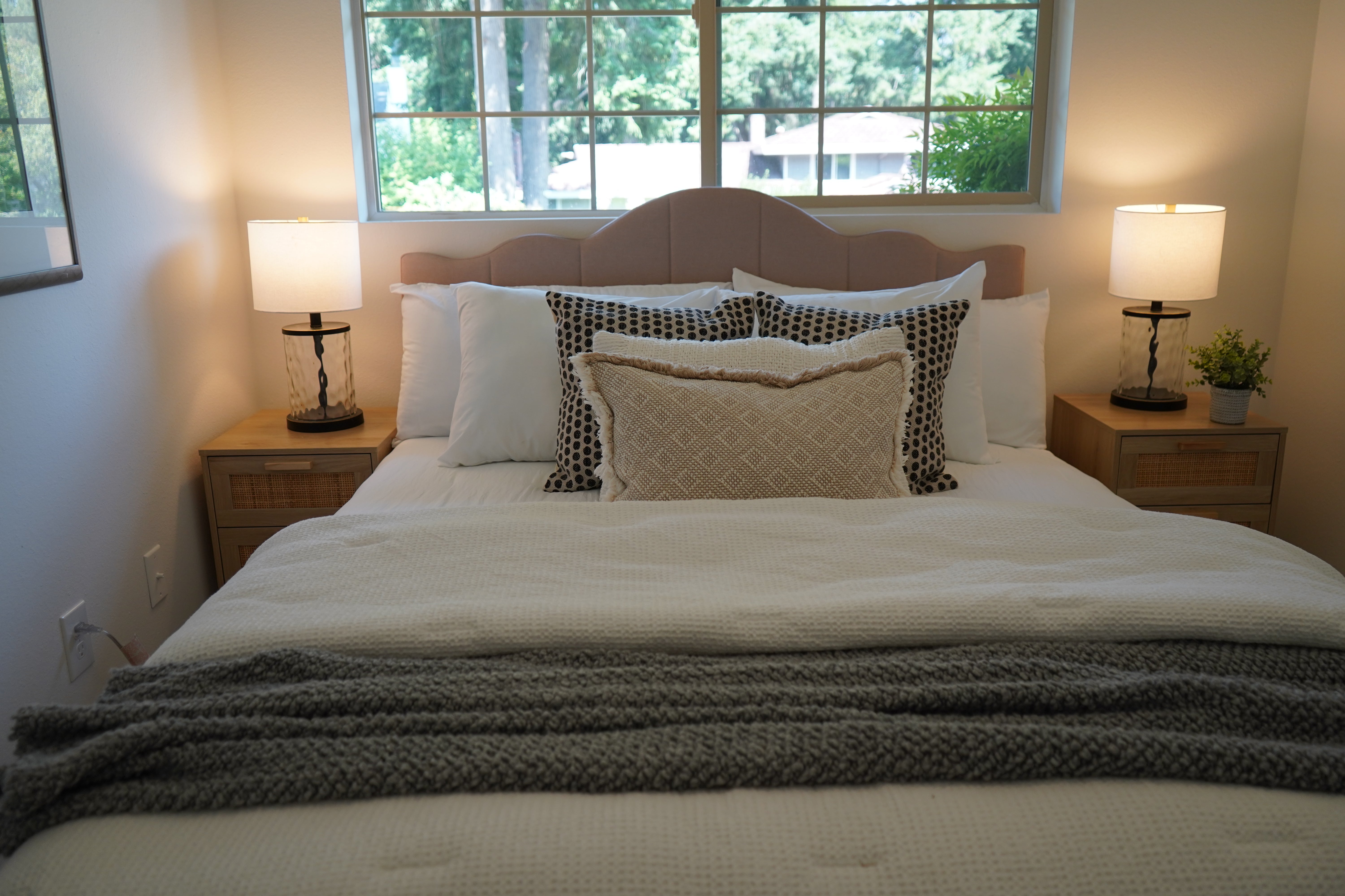 Bedroom with a neatly made bed, two lamps on nightstands, and a window in the background.