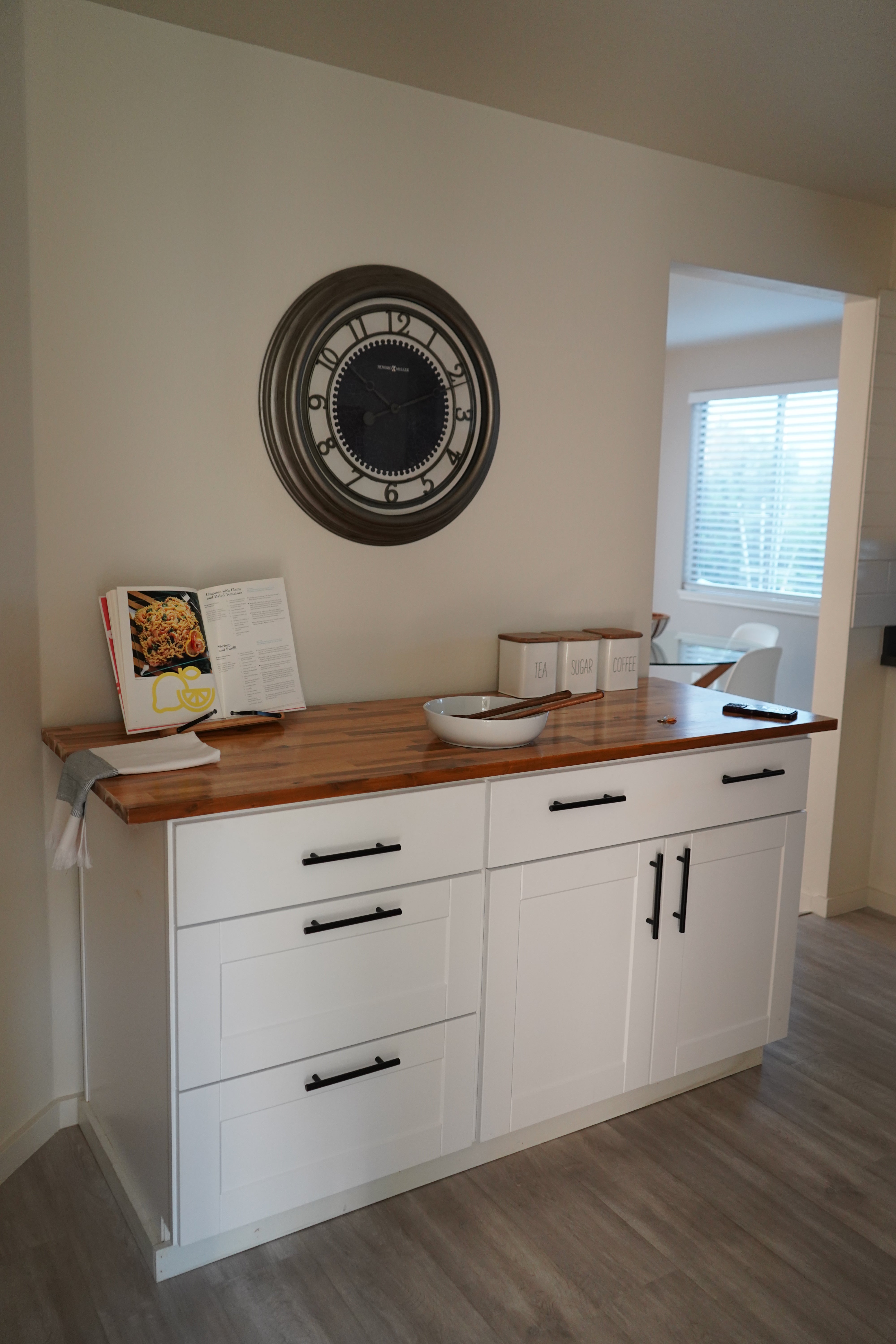 White cabinet with black handles in a room with a clock on the wall.