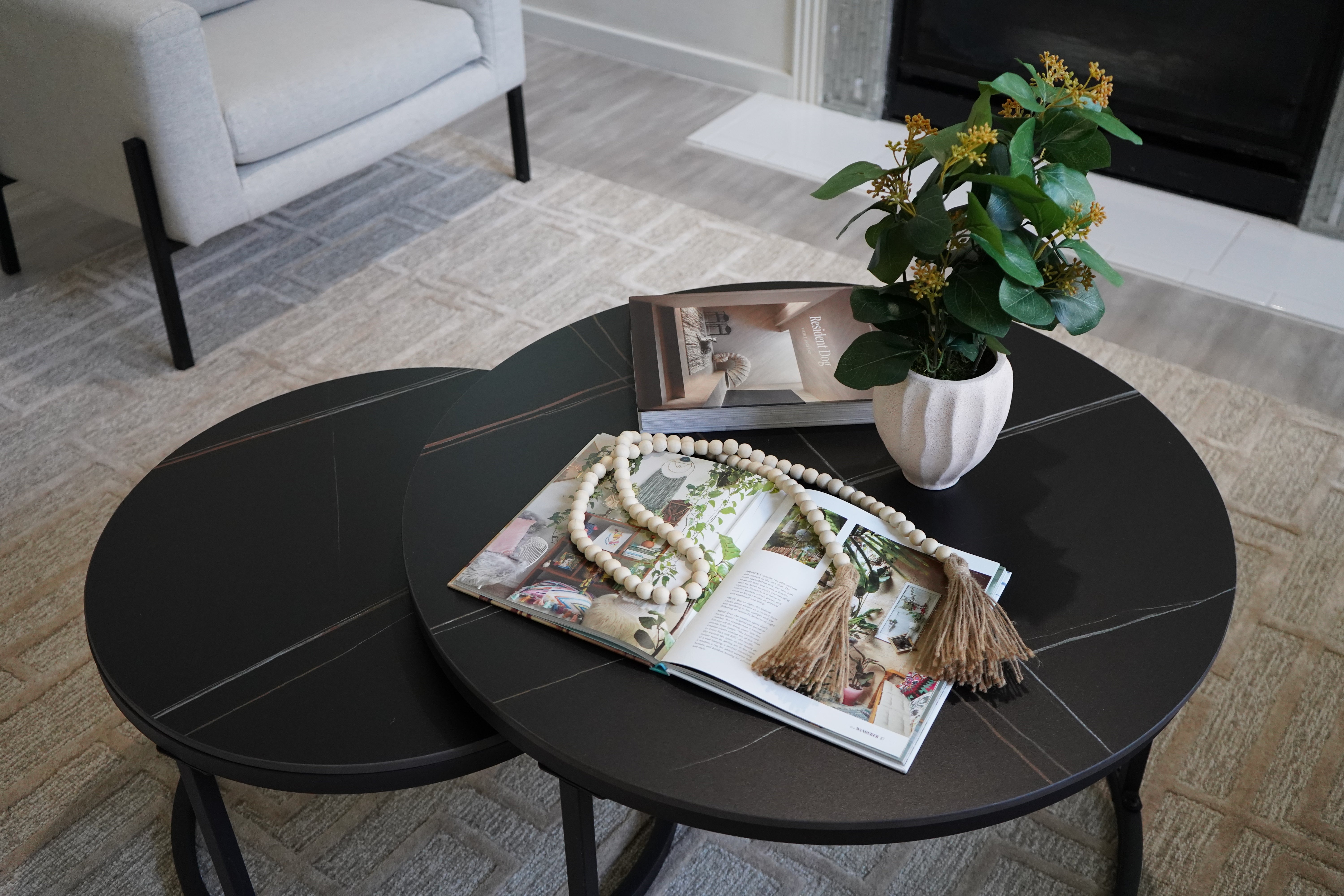 Round black coffee table with magazines and a vase of flowers in a living room setting.