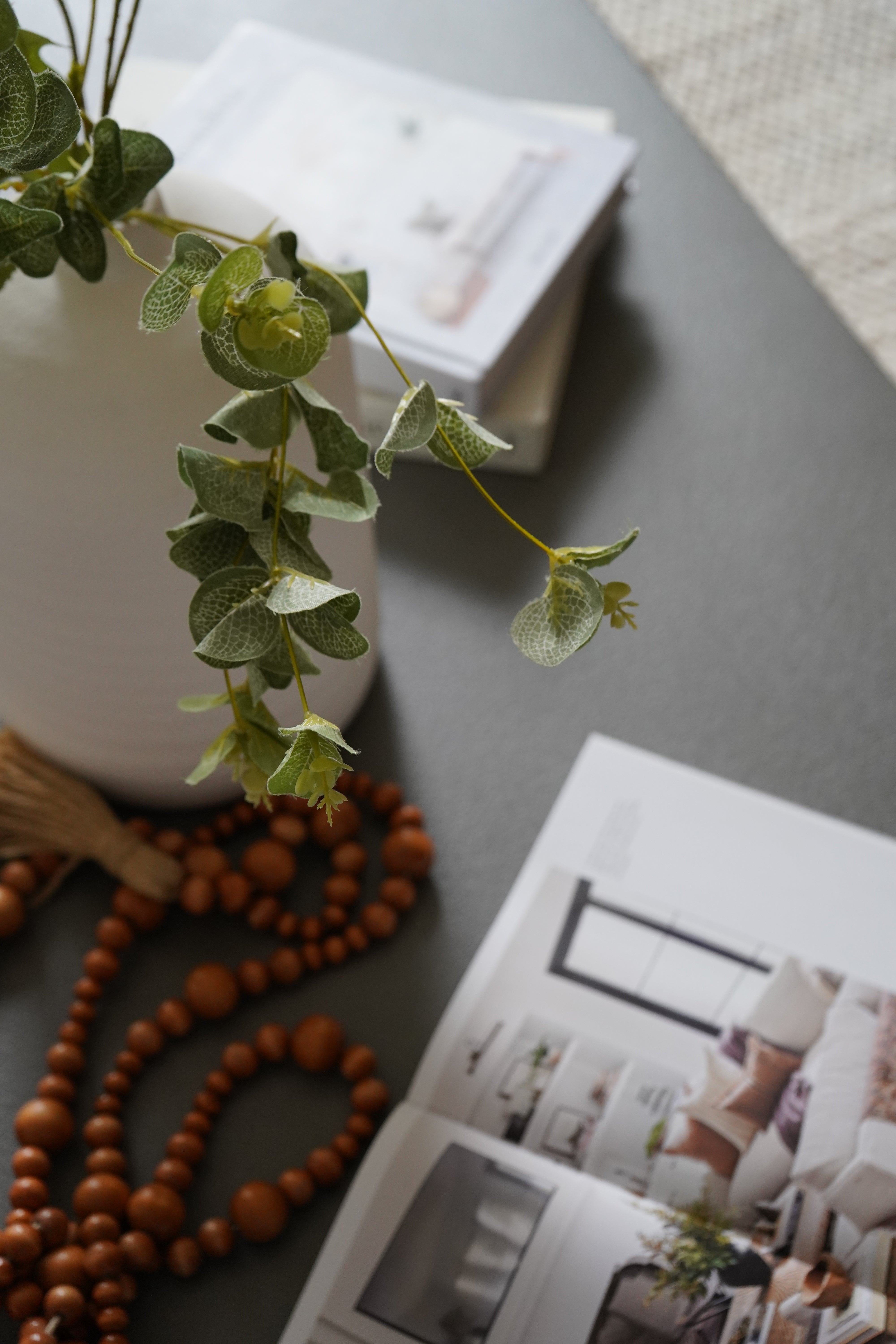 Decorative items including a string of beads and a small plant on a surface with a magazine in the background.