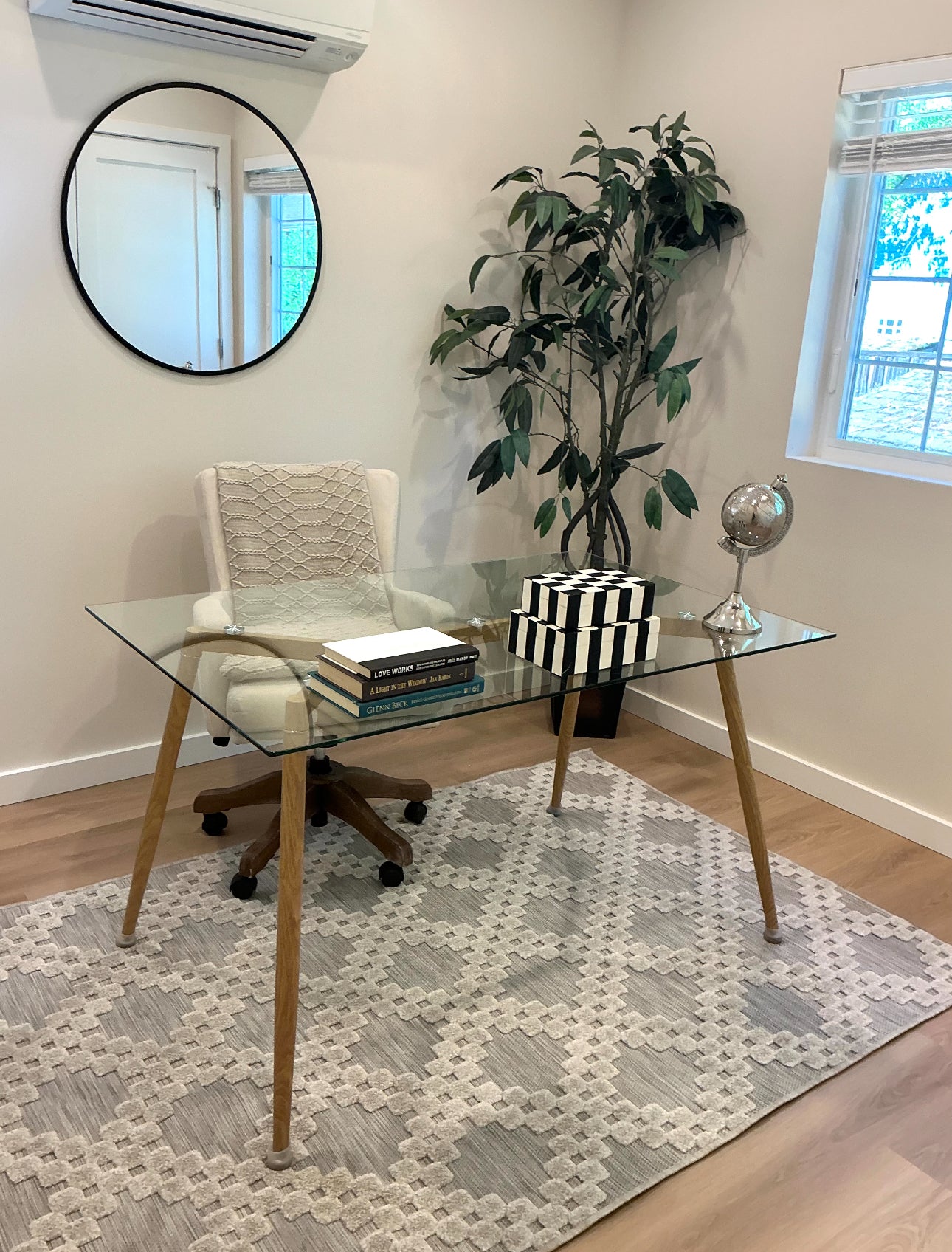 Home office with glass desk, chair, books, plant, and decor items.