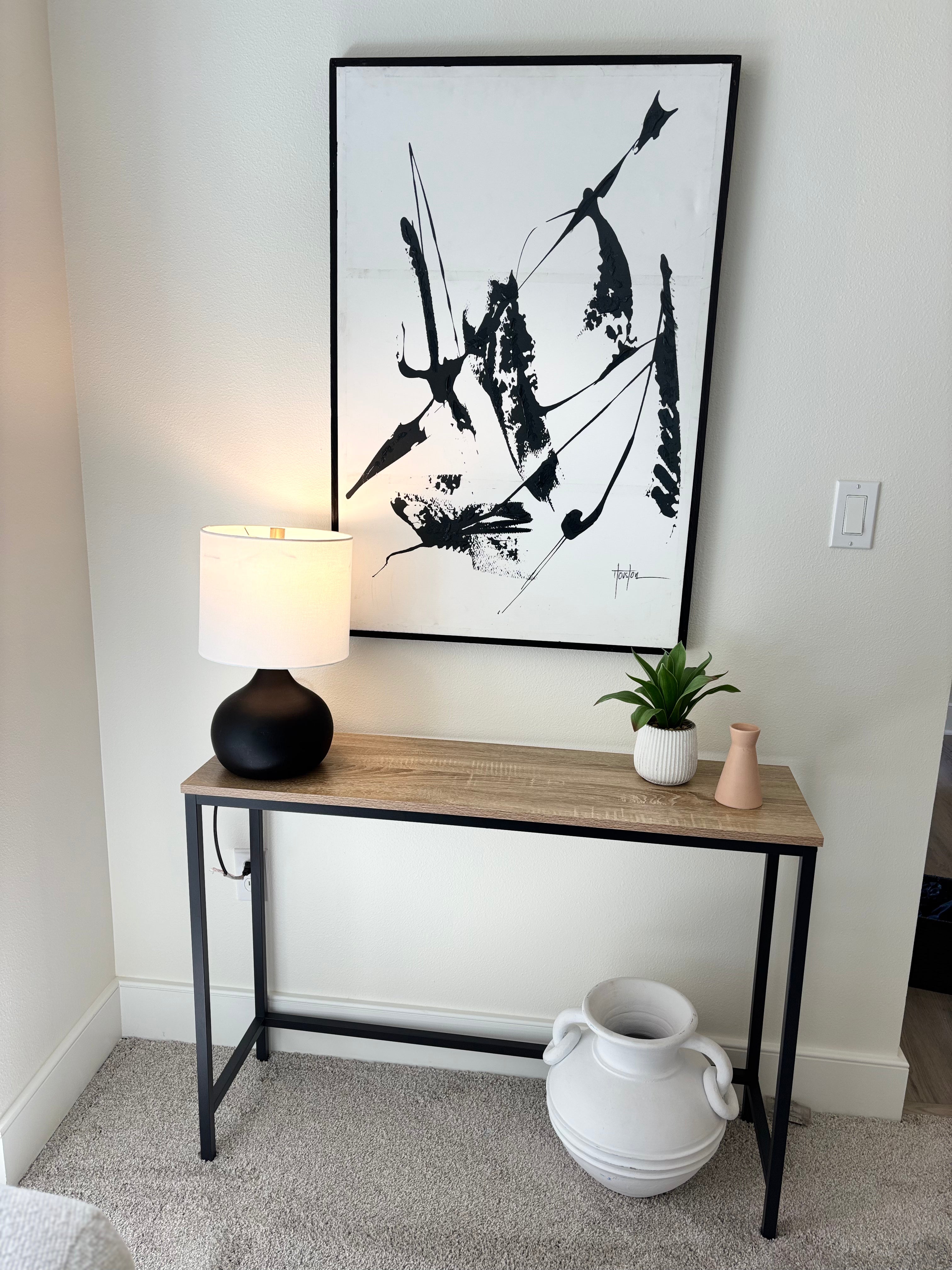 Console table with decorative items against a wall with framed abstract art.
