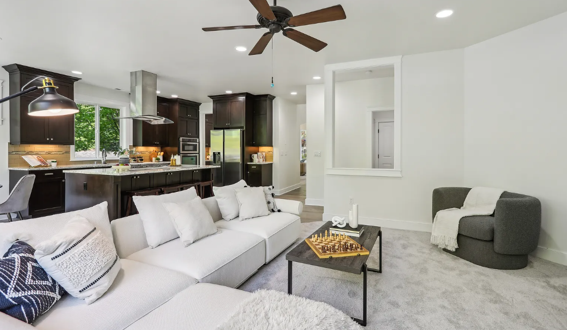 Modern living room with white sectional sofa, coffee table, and kitchen in the background.